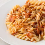 A bowl of pasta coated in rich, tangy pizza sauce garnished with oregano