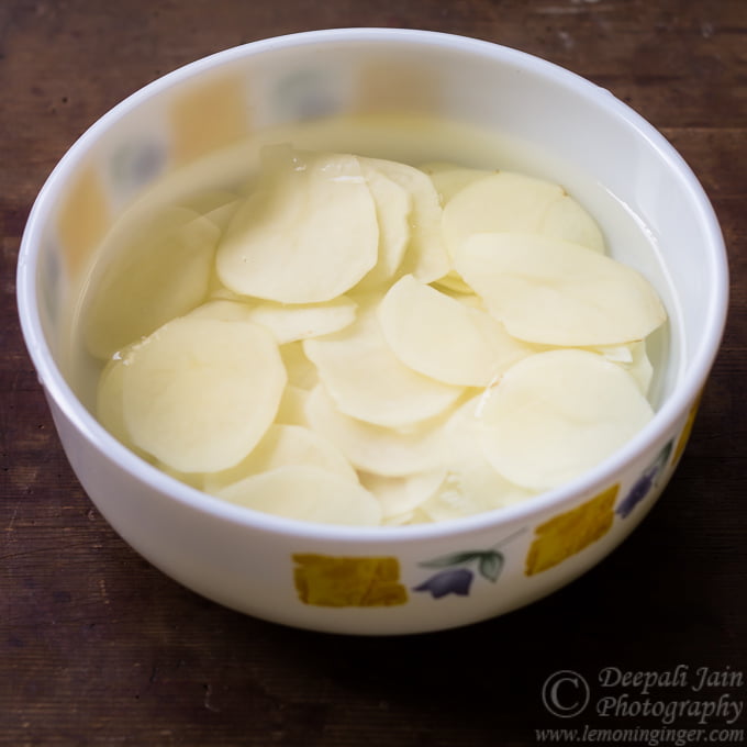 Potato slices soaking in a bowl of water to remove starch