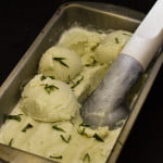Several scoops of basil ice cream in a ice cream tray, with fresh basil leaves on the top