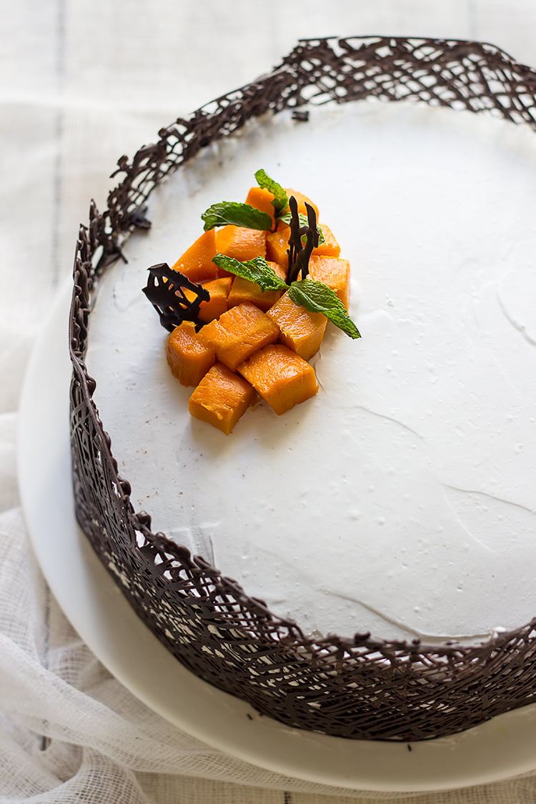 A whole eggless mango white cake placed on a plate, ready to be sliced