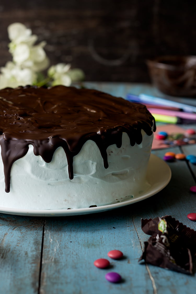 A colorful M&M Pinata Cake topped with chocolate ganache
