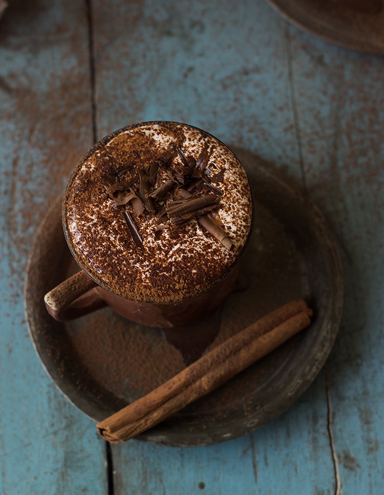 A mug of hot chocolate with a cinnamon stick and chocolate shavings on top