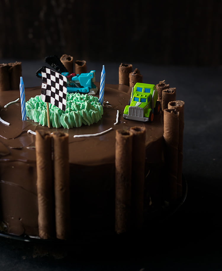 A fabulous race track cake with two toy car at the top