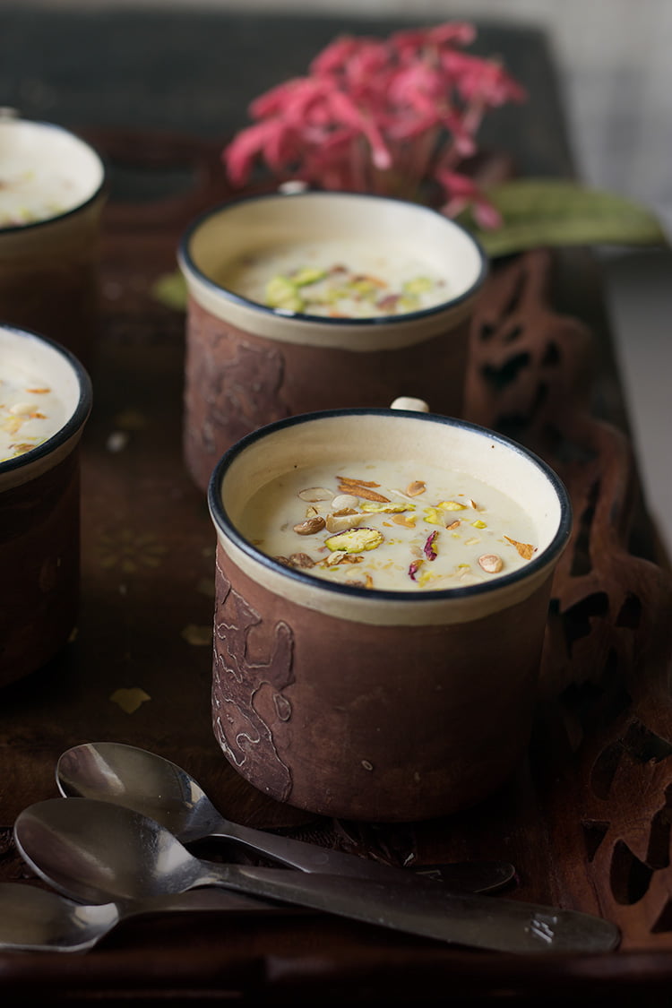 A cup full of creamy Gur ki Kheer garnished with sliced almonds and pistachios