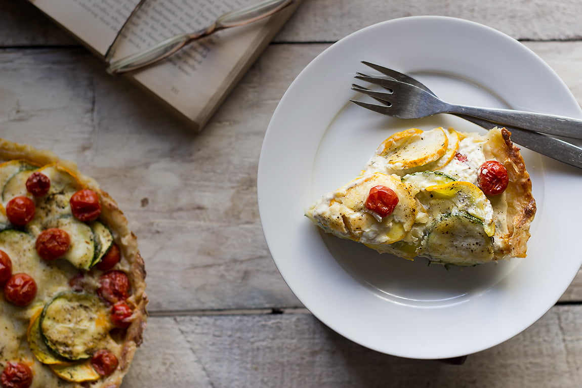 Serving Tomato Zucchini Tart on a white plate, ready to dig in