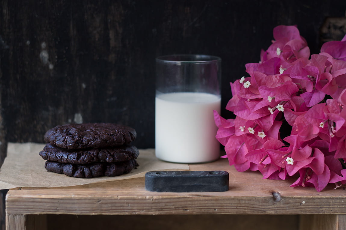 A glass of milk next to a pile of double chocolate chip cookies