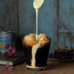 A tall glass of iced coffee with a frothy top and a straw