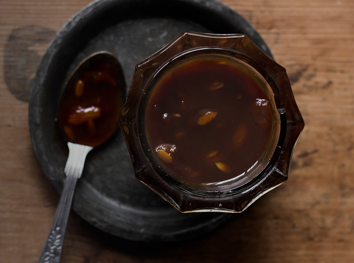 A jar of homemade Sweet Imli Chutney with a spoon sticking out, ready to be used