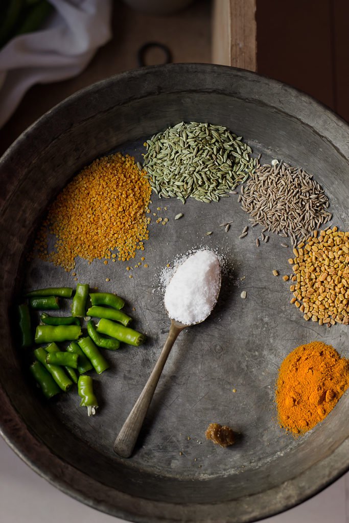 Fresh green chillies, mustard seeds, and spices arranged on a wooden board, ready to make the pickle