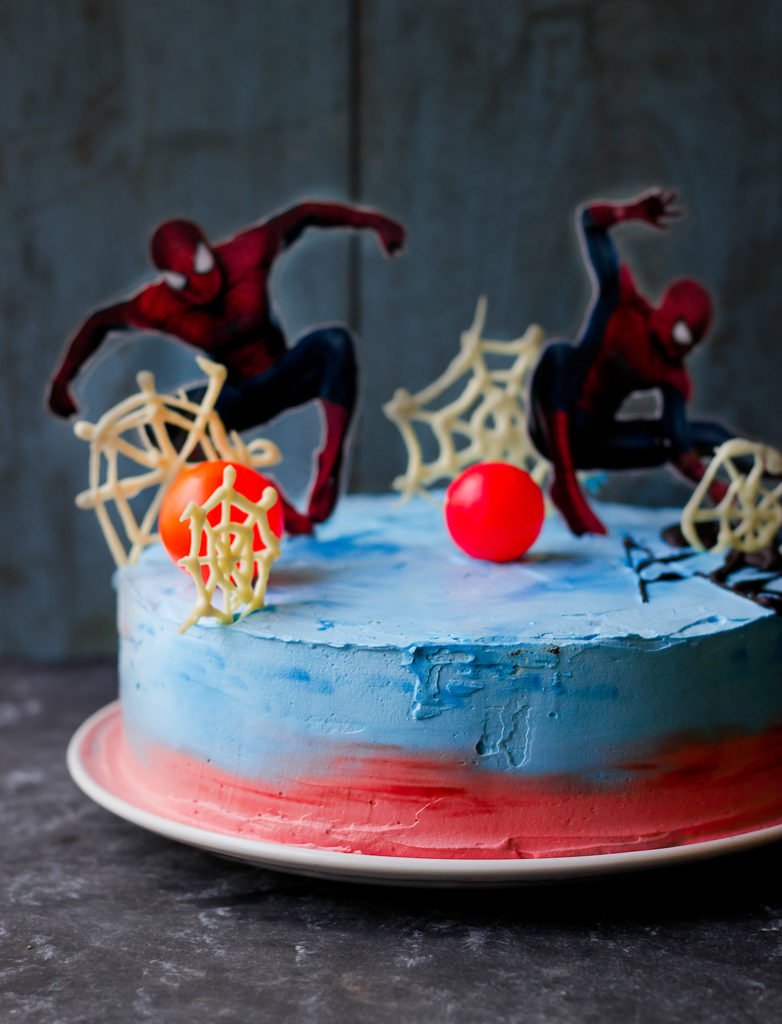 A homemade Spiderman cake with detailed red and blue icing, featuring Spiderman's iconic web design on top