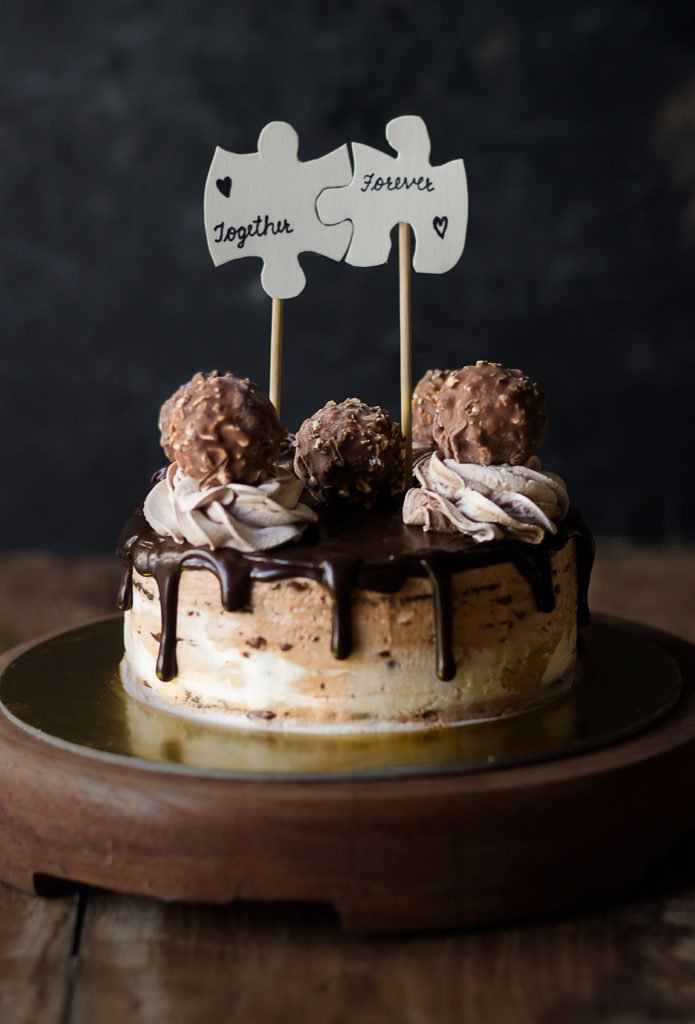 A whole Eggless Ferrero Rocher Cake surrounded by Ferrero Rocher chocolates, showcasing its decadent and luxurious appeal