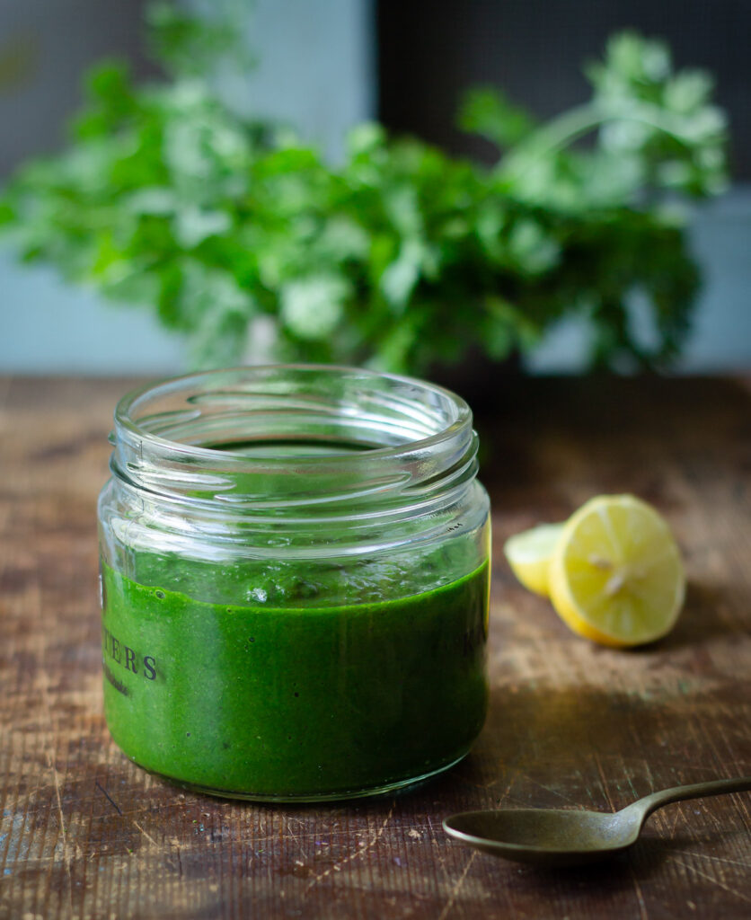 Side view of dhaniya pudina chutney with lemon and spoon at the side