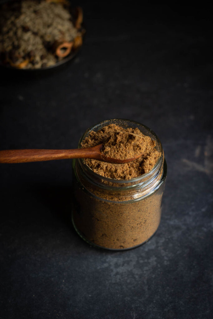 A spoonful of homemade garam masala taken out from a jar