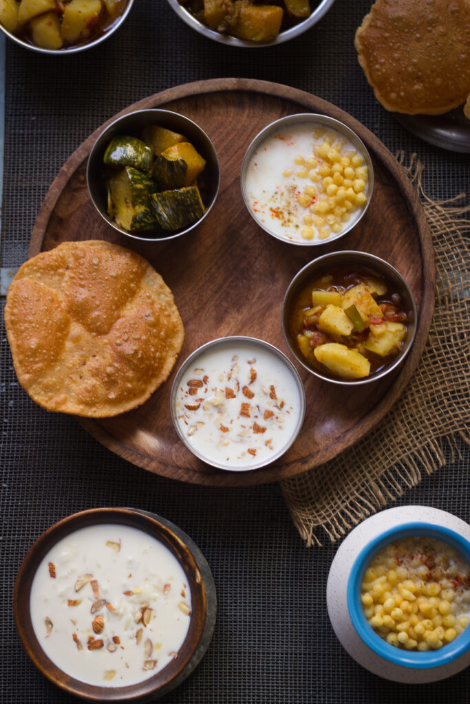A plate of puris, golden and puffed, alongside a bowl of raita on the Satvik Thali