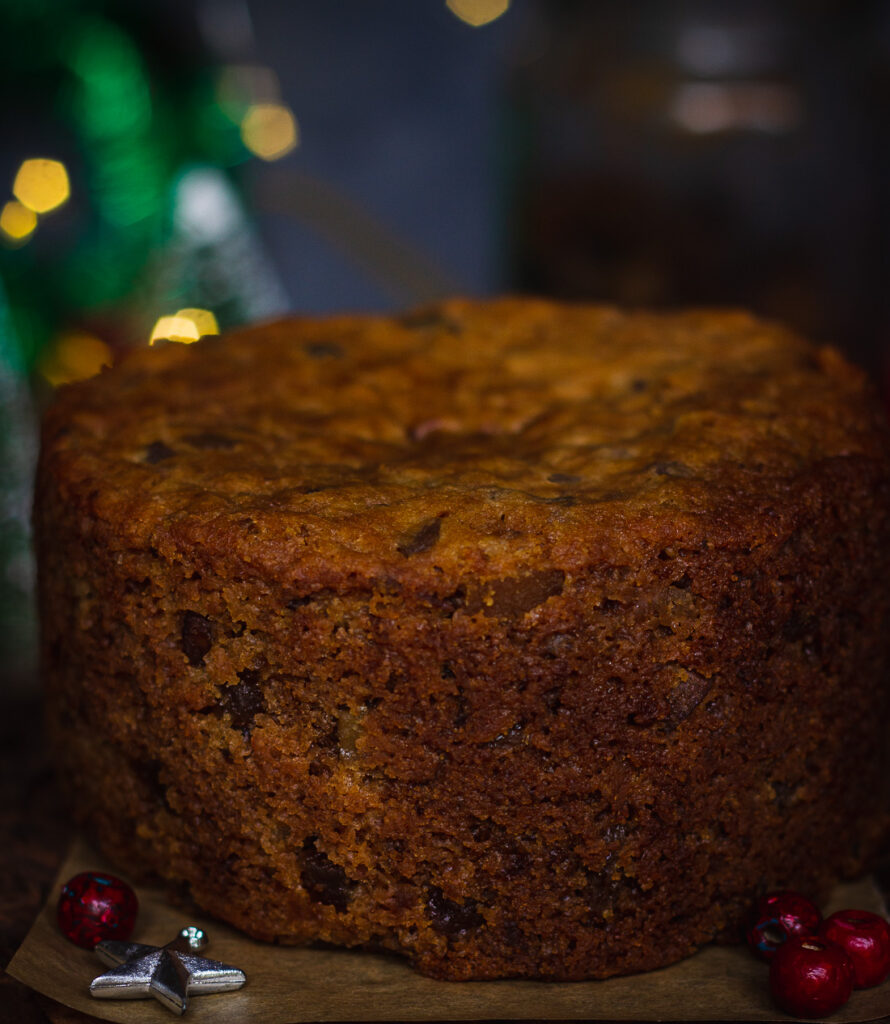 A freshly baked brandied fruit cake cooling on a wire rack, surrounded by ingredients